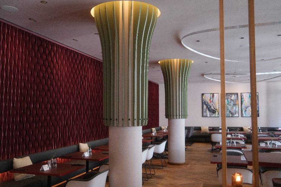 Modernes Restaurantinterieur mit einzigartigen grünen Säulen, roten strukturierten Wänden, Holzfußböden und kunstvoller Wanddekoration.